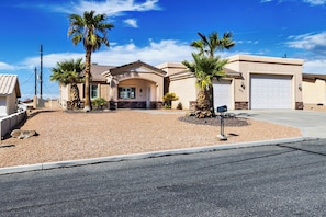 A two-story house with a garage, surrounded by a gravel driveway and palm trees. - Lake Havasu Pool Retreat~3BR~Boat Parking~Sleeps 6 (Lake Havasu City)