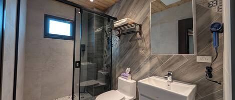 Un baño moderno con cabina de ducha de vidrio, inodoro blanco, lavabo con espejo y toallero.