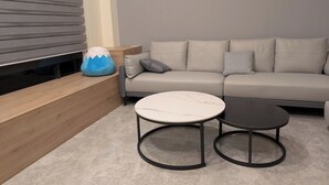 A modern living room with a sofa, two round tables, a wooden bench, and a decorative blue and white cushion. - Johnson Bros Inn Taitung (Taitung)