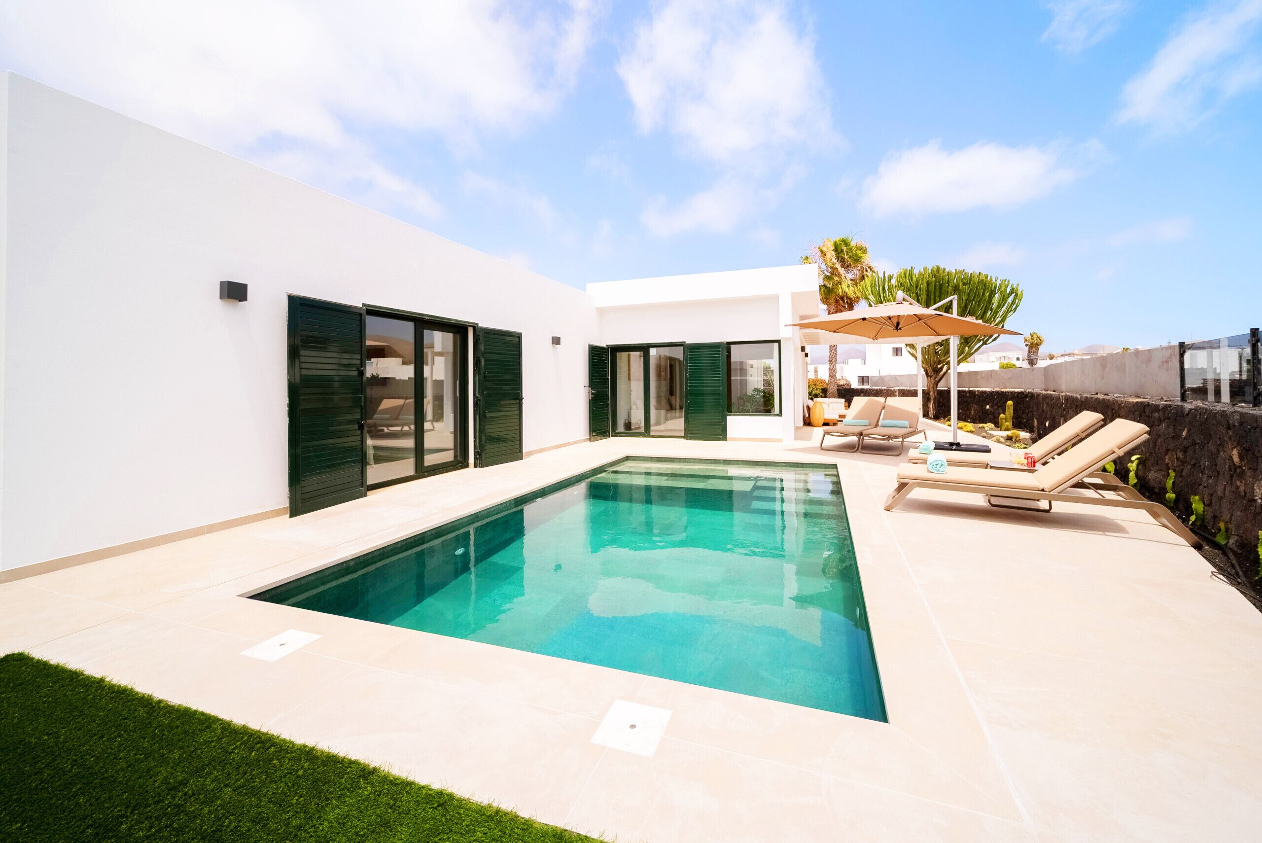 A modern house with a swimming pool, outdoor seating, and a well-maintained lawn.