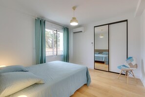 A bedroom with a bed, a chair, a window with curtains, an air conditioning unit, and a mirror. - Capbreton Beach, apartment for 6 people (CAPBRETON)