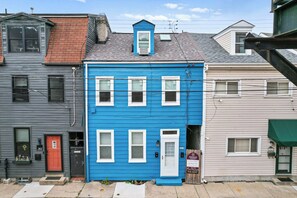 A row of townhouses with a blue house in the center, a red door, and a 'For Rent' sign. - Trendy 2BR Near Carson Street | Free Parking (Pittsburgh)