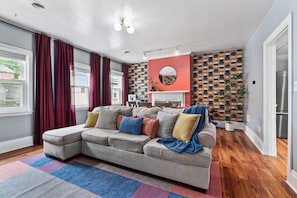 A modern living room with a sectional sofa, a patterned wall, and a fireplace. - Trendy 2BR Near Carson Street Pets OK (Pittsburgh)