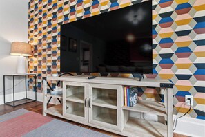 Una sala de estar con un televisor de pantalla plana grande, un mueble de madera con puertas de cristal y una pared con estampado.
