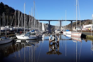 A marina with multiple sailboats docked, a bridge in the background, and calm water reflecting the boats. - Le clos Rucharet - SAINT CARREUC (SAINT CARREUC)