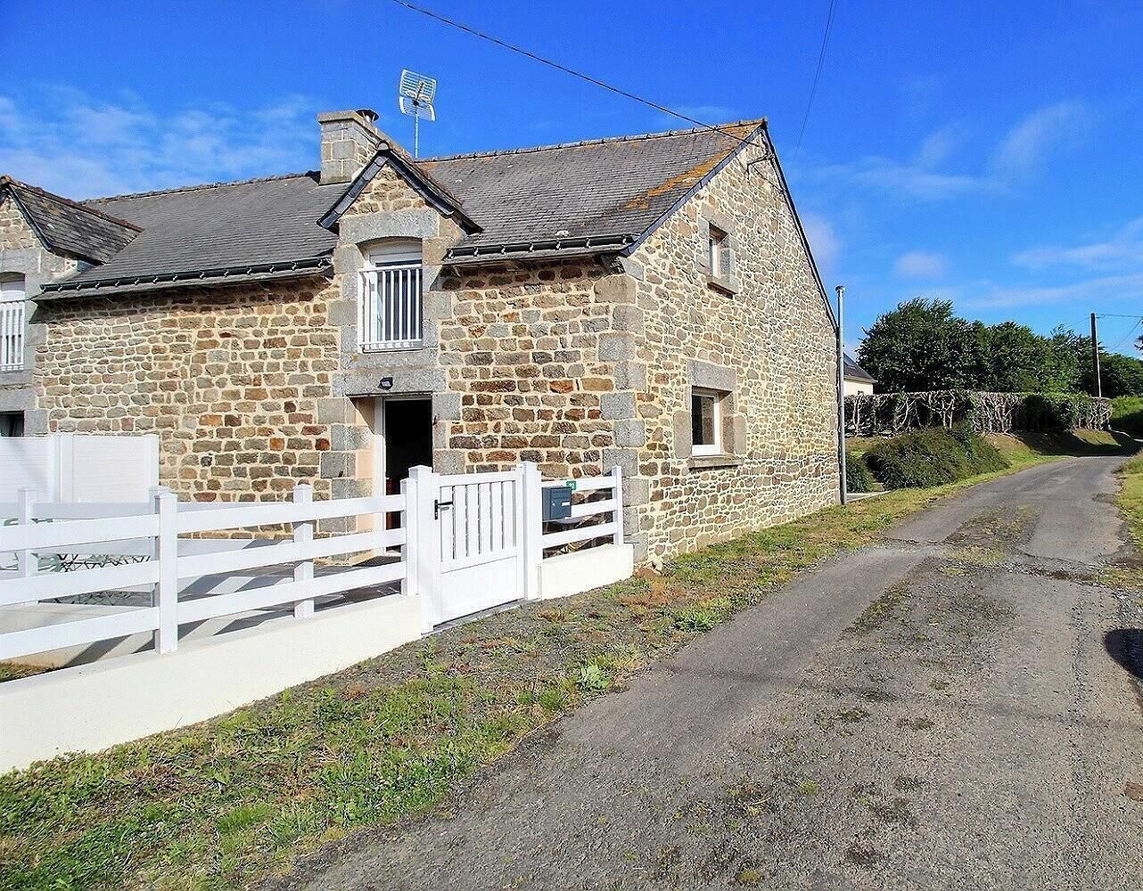 Un edificio de piedra con cerca blanca, camino de grava y cielo despejado.