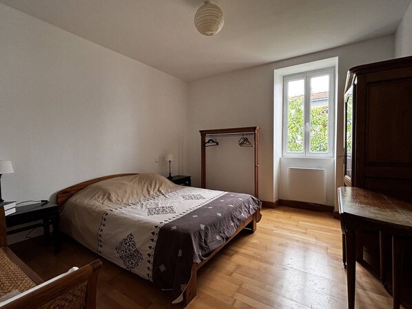 Ein Schlafzimmer mit Bett, Nachttisch, Lampe, Kleiderschrank und einem Fenster mit Aussicht.