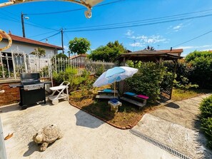 Ein Garten mit Grill, Sitzgelegenheit im Freien und einer Pergola mit Sonnenschirm.