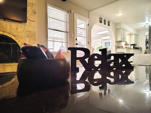 A modern living room with a fireplace, a large window with blinds, and a 'Relax' sign on the floor. - El Paso's Premiere Short to Mid Term Rental (El Paso)