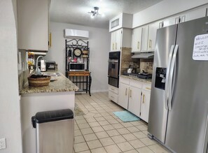 Una cocina con un refrigerador de acero inoxidable, un microondas y una estufa. Hay un reloj en la pared y una cesta de fruta en la encimera.