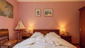 Una camera d'albergo con un letto, due abat-jour, un comodino in legno, una sedia e un quadro appeso al muro.