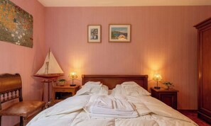 Ein Hotelzimmer mit einem Bett, zwei Nachttischlampen, einem Holznachttisch, einem Sessel und einem Bild an der Wand.