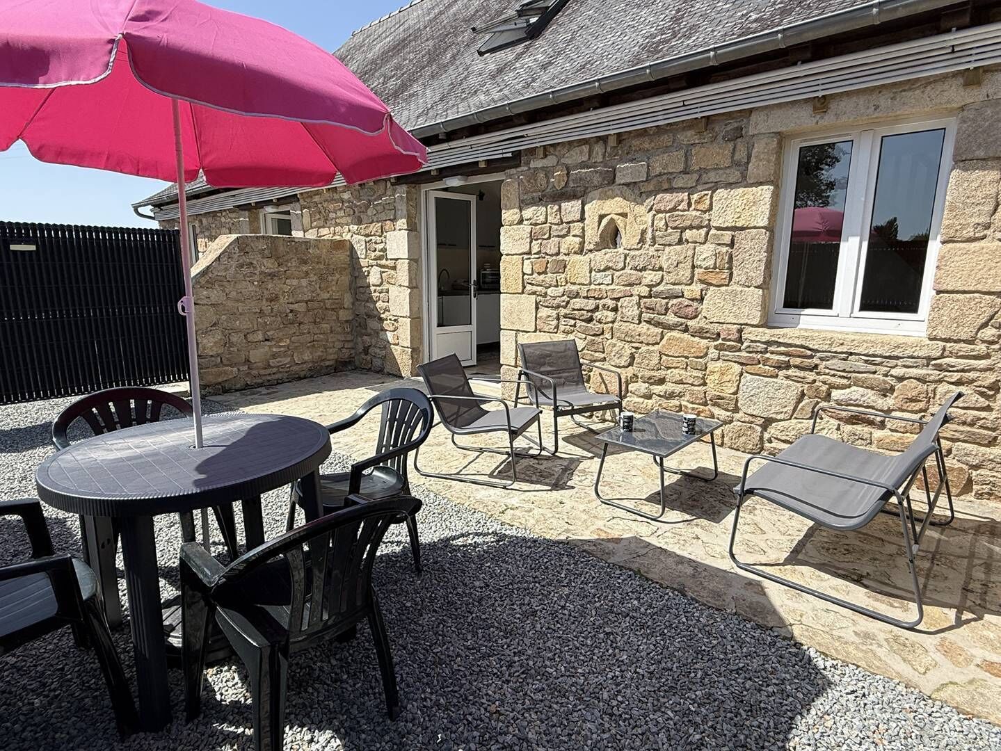 A stone building with a patio area featuring a round table, four chairs, and a large umbrella.