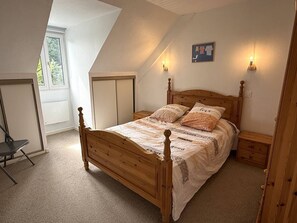 Ein Schlafzimmer mit schrägem Dach, einem hölzernen Bett, Nachttischen, einem Sessel und einem Fenster.
