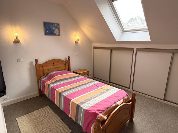 A bedroom with a sloped ceiling, a skylight, a bed with a striped bedspread, two wall-mounted lights, and a small bedside table. - NEW LISTING, Domaine de KER-PAULT, between St Cast and Matignon, 3-room cottage 5 minutes from... (MATIGNON)