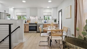 Eine moderne Küche mit weißen Schränken, ein Essbereich mit rundem Tisch und Stühlen sowie eine Treppe mit Metallgeländer.
