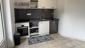 Una cocina compacta con armarios blancos, encimera negra, lavavajillas de acero inoxidable y una alfombra estampada.