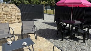 Un patio al aire libre con una mesa, sillas, un paraguas rosa y un muro de piedra.