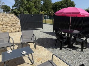 An outdoor patio with a table and chairs, a pink umbrella, and a stone wall. - NEW, Domaine de KER-PAULT, between St Cast and Matignon, studio apartment 5 minutes from the beaches (MATIGNON)
