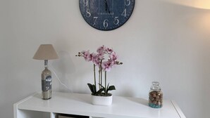 Un reloj de pared, una lámpara, una orquídea en maceta y un tarro sobre una consola blanca.