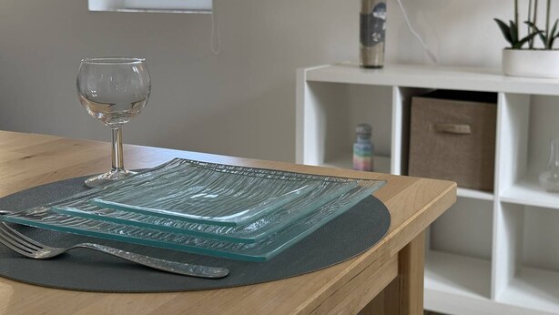 Una mesa con un vaso, un tenedor, un cuchillo y un mantel individual de vidrio.