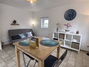 A modern living room with a dining table, sofa, and a decorative clock on the wall. - NEW, Domaine de KER-PAULT, between St Cast and Matignon, studio apartment 5 minutes from the beaches (MATIGNON)