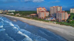 Ein Strandhotel mit mehreren Hochhäusern, einem Sandstrand und Meereswellen.