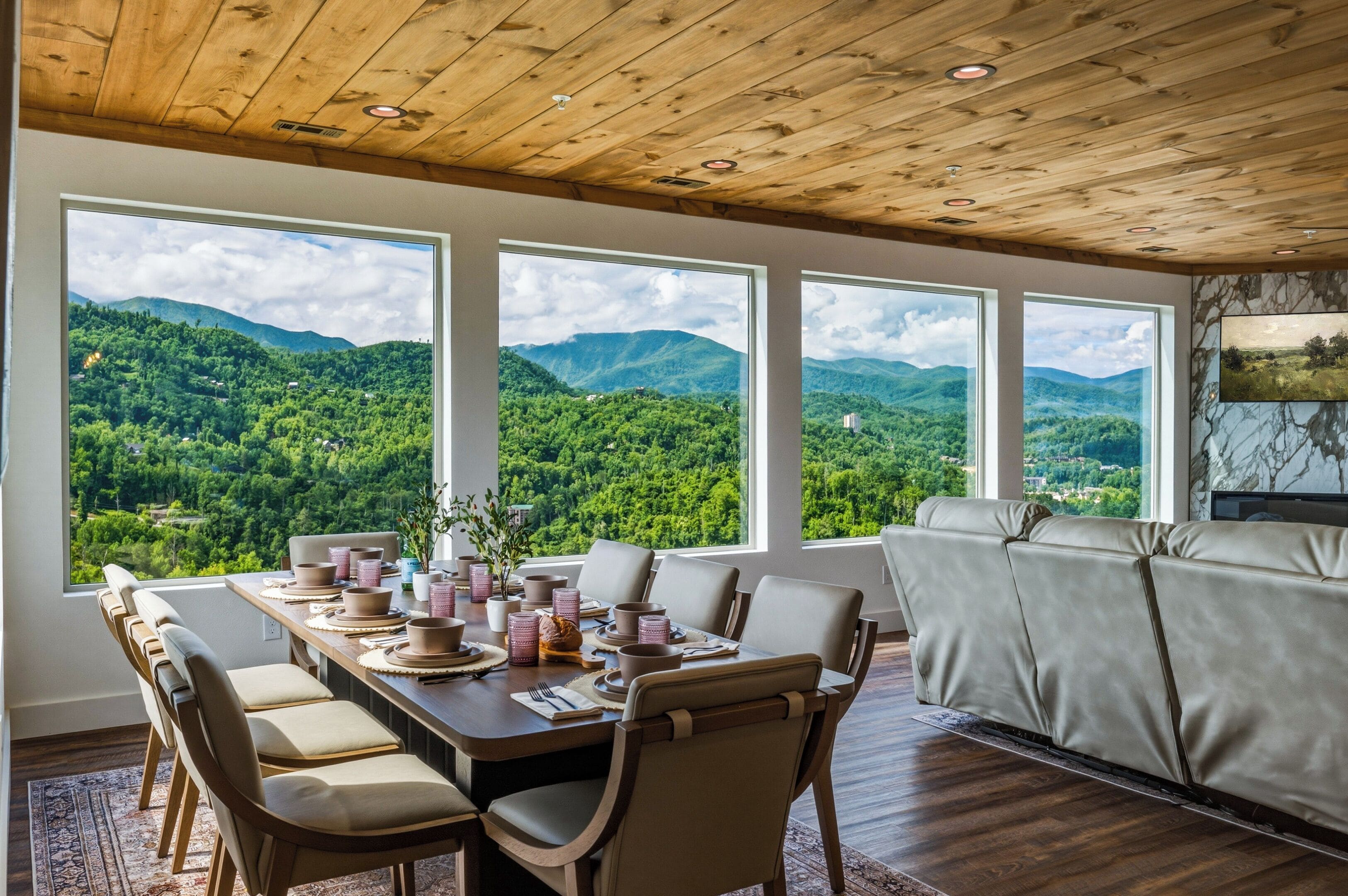 A dining area with a table set for four, large windows offering a view of a mountainous landscape, and a sofa in the adjacent living area.