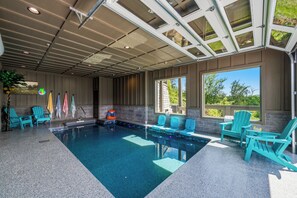 Une piscine intérieure à l’eau d’un bleu cristallin, entourée de chaises turquoise, avec vue sur la verdure environnante.