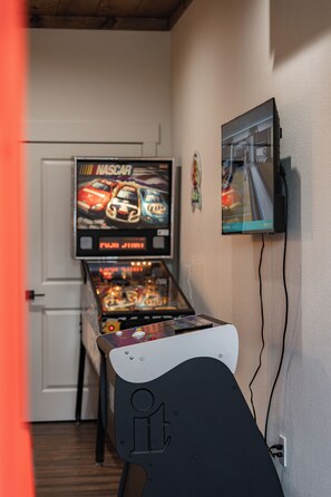 Eine Flipper Maschine mit NASCAR-Mottiven, ein an der Wand befestigter Fernseher und eine Tür im Hintergrund.