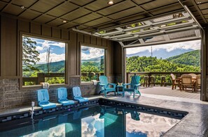 Ein Poolbereich mit Stühlen und Tischen, Blick auf Berge und eine überdachte Terrasse.