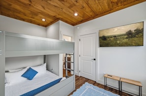 Ein Zimmer mit einem Etagenbett, einer Tür, einem Bild und einem kleinen Holztisch.