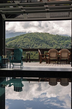 Une terrasse avec des fauteuils Adirondack et une table, offrant une vue sur une montagne boisée.