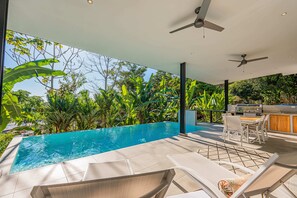 Ein Poolbereich mit Liegestühlen, einem Tisch, Deckenventilatoren und einem Grill.