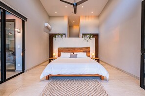 Ein modernes Schlafzimmer mit einem großen Bett, Nachttischen, einem Deckenventilator und Blick ins Freie.