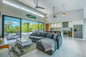 Ein modernes Wohnzimmer mit einem grauen Ecksofa, einem Glastisch und einer Küchenzeile mit Edelstahlgeräten.