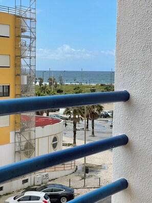 Ein Balkon mit Blick auf den Ozean, ein gelbes Gebäude und eine von Palmen gesäumte Straße.