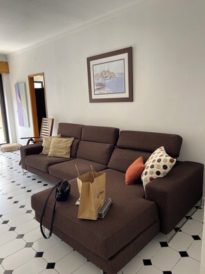 Ein braunes Sofa mit Kissen, ein gerahmtes Bild an der Wand und eine Einkaufstasche auf dem Boden.