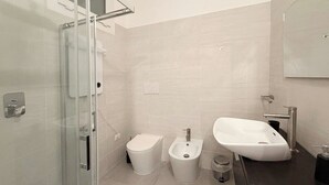 Et moderne badeværelse med en glas brusekabine, toilet, bidet og håndvask.