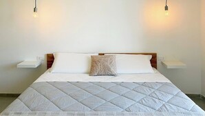 En pænt redt seng med et quiltet dynebetræk, to puder og et natbord med en lampe.