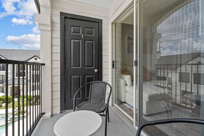 A balcony with a black door, a wicker chair, a white table, and a glass door leading to an interior space. - 2302 Cortland (Houston)