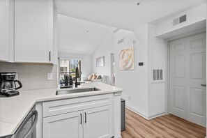 A modern kitchen with white cabinetry, a large island, and a view to the living area. - 2302 Cortland (Houston)