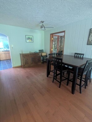 A dining area with a wooden table and chairs, a ceiling fan, and a stone-framed door.