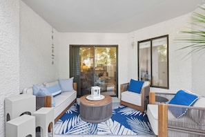 A sunlit patio with a sofa, two chairs, a round table, and a view through a glass door. - Ground level Villa with Community Indoor & Outdoor Pool + Free Activities! (Hilton Head Island)