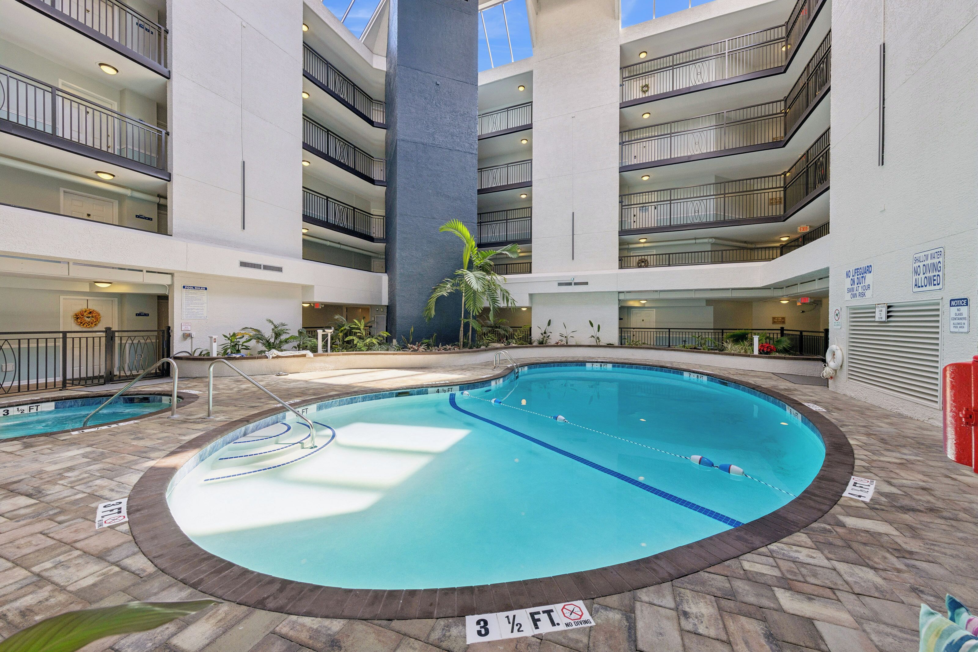 An indoor swimming pool with a 3 1/2 ft depth, surrounded by a multi-level building with balconies and a central pillar.