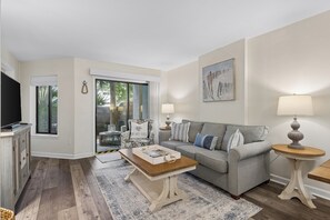 A living room with a grey sofa, wooden coffee table, and a TV on a cabinet. - Ground level Villa with Community Indoor & Outdoor Pool + Free Activities! (Hilton Head Island)