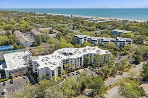 A multi-story hotel with a rooftop pool, surrounded by trees and a beach view. - Ground level Villa with Community Indoor & Outdoor Pool + Free Activities! (Hilton Head Island)