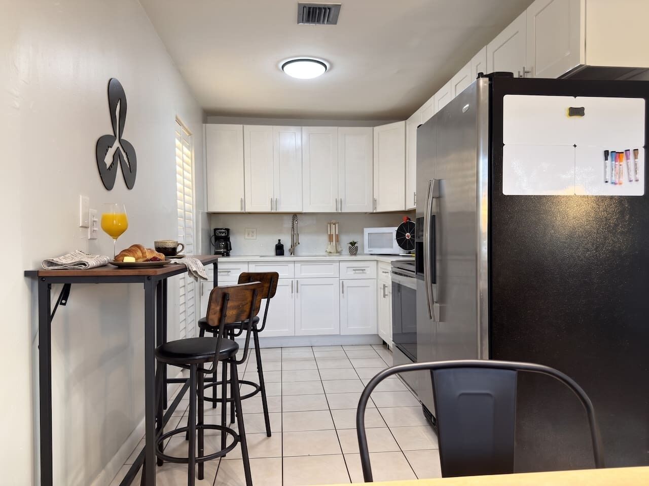 A compact kitchen with white cabinets, a black refrigerator, and a small dining area with two stools.