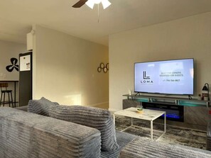 A modern living room with a sofa, a coffee table, a flat-screen TV, and a ceiling fan. - Casa Hard Rock - Sleeps 14+Games+15 min to FTL (Miramar)