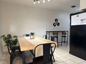 A dining area with a long table, chairs, a refrigerator, and a wall-mounted light fixture. - Casa Hard Rock - Sleeps 14+Games+15 min to FTL (Miramar)